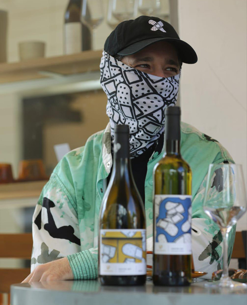 Israeli artist Dede sitting at a table with bottles of the Inspire Art wine collection he created in collaboration with Tepenberg winery